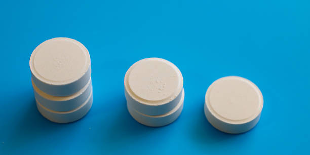istock Three stacks of white round tablets of different heights are arranged on a bright blue background. Medical image illustrating a decrease in dosage or stages of treatment. 2212995333
