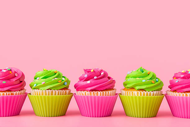 Colorful cupcakes with frosting and sprinkles in row on pink background