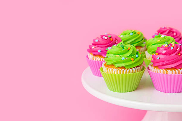 istock Colorful cupcakes with swirled frosting and sprinkles on pink background 2212997077