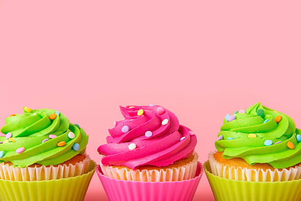 istock Three colorful cupcakes with bright icing and sprinkles on pink background 2212997091