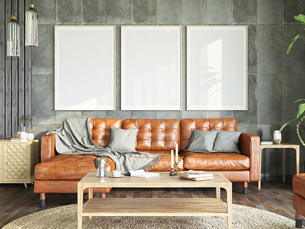 Woman sits on the window sill and using phone in modern living room with leather couch on brick wall background. Home coziness and leisure time with gadgets