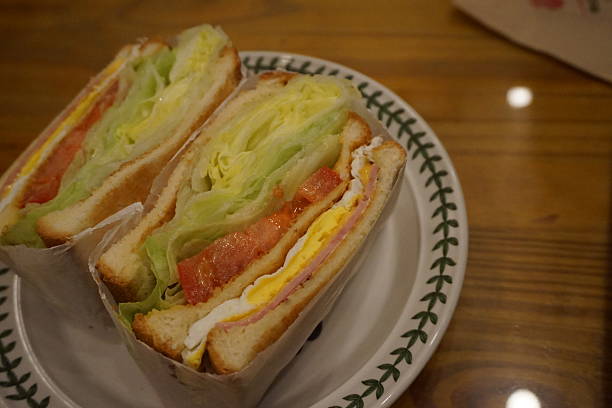 istock A freshly made layered sandwich featuring ham, egg, tomato, lettuce, and mayonnaise between slices of toasted bread, elegantly wrapped and placed on a decorative plate. 2213008311