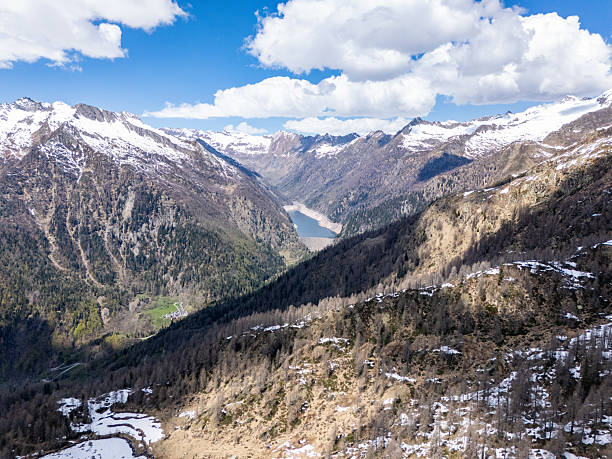 Breathtaking view of snow-covered peaks stretching across a vast mountain range. Majestic clouds hovering above rugged terrain. Idyllic natural landscape of towering mountains.