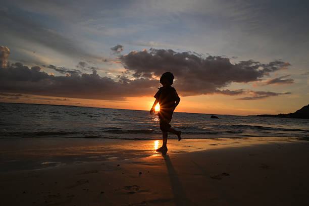 Little red-haired boy stands in the sea and looks on the sun
