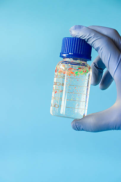Stock photo showing close-up view of sample bottle containing microplastics floating in water. Microplastics can measure between 1 micron to 5 millimeters and are insoluble in water, unfortunately, they can leak harmful chemicals which can contaminate air, water and food and so cause harm to the health of the environment and human health.