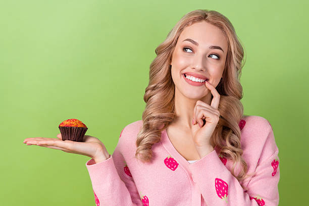Portrait of cute cunning tricky minded lady finger touch lips arm hold muffin look empty space isolated on green color background