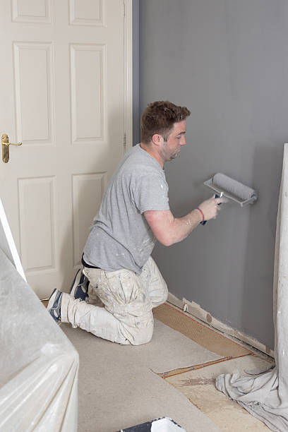 istock Young, self employed and skilled Painter & Decorator overcoming the disability of having one hand, decorating a domestic living room with a roller 2213021809