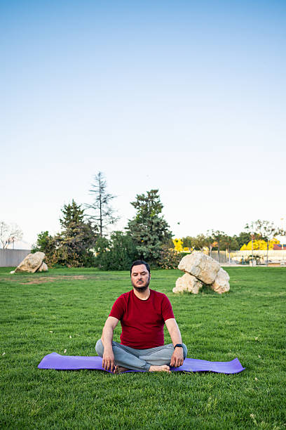 Meditating man in a serene park setting during early evening hours