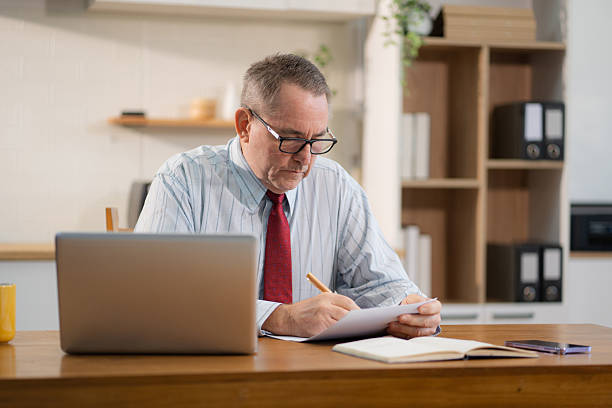 istock Mature male entrepreneur working online from home, managing documents and laptop at kitchen desk.  modern small business owner embracing remote work. 2213027708