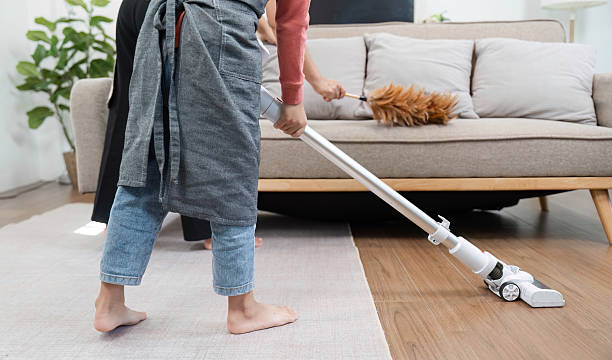 istock Home Cleaning and Teamwork. A young boy vacuums the floor while his mother assists with dusting. 2213029782