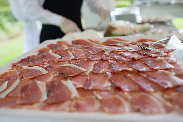 Prosciutto slices arranged on a platter, with catering staff serving at a wedding reception buffet.