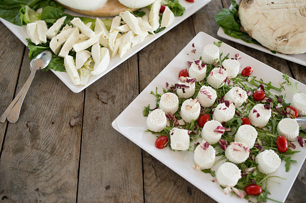 Close-up of Italian mozzarella and ricotta cheese served with greens and cherry tomatoes on a rustic table.