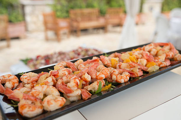 Close-up of a seafood platter with fresh shrimp garnished with citrus and greens, served at an outdoor wedding or reception buffet.