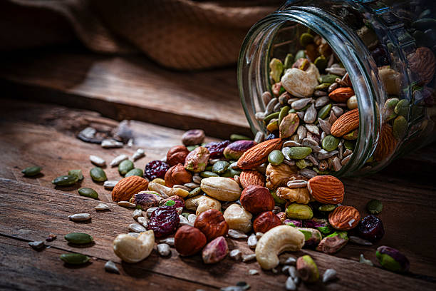 Trail mix: nuts and seeds spilling out from a glass jar on rustic wooden table