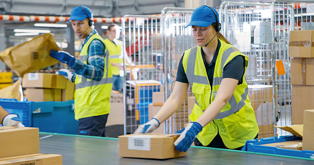 istock Female and Male Employees Sorting and Loading Parcels, Packages, Cardboard Boxes on a Conveyor Belt in a Postal Office or Retail Shop Warehouse Facility, Ensuring Smooth Logistics Operations 2213036827