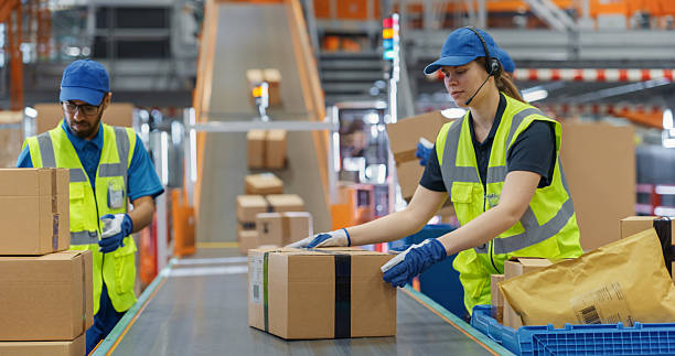 istock Diverse Workers in Safety Vests Loading Parcels Onto a Conveyor in a Modern Sorting Center Facility. People Working Together as a Team in Logistics and Postal Service Operations 2213037572