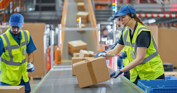 istock Experienced and Young Employees Sort Packages and Load Boxes on a Conveyor Line. Diverse Portrait of Employees at Work in a National Postal Service Facility or a Modern Retail Warehouse Building 2213037648