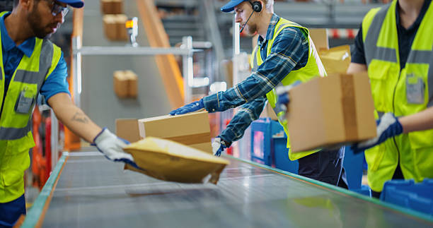 In a Modern Sorting Center Facility, Diverse Workers in Safety Vests Loading Parcels Onto a Conveyor, Efficiently Working Together as a Team. Logistics and Postal Service Operations In a Modern Sorting Center Facility, Diverse Workers in Safety Vests Loading Parcels Onto a Conveyor, Efficiently Working Together as a Team. Logistics and Postal Service Operations satisfaction stock pictures, royalty-free photos & images