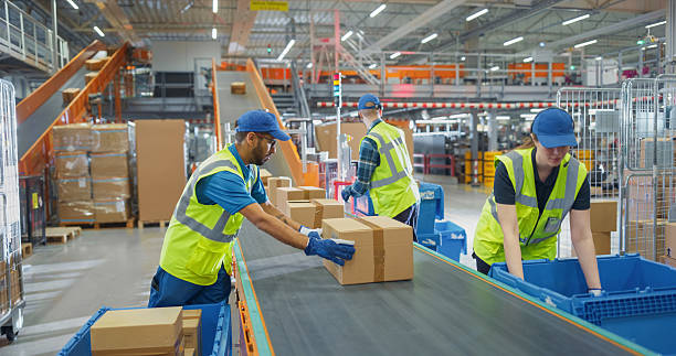 istock Workers in High-Visibility Vests Redirect Packages Along a System of Conveyor Belts in a Distribution Hub. Male and Female Working in Large-Scale Retail E-Commerce Operation or Logistics Service 2213037798