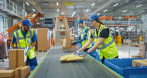 istock Female and Male Employees Sorting and Loading Parcels, Packages, Cardboard Boxes on a Conveyor Belt in a Postal Office or Retail Shop Warehouse Facility, Ensuring Smooth Logistics Operations 2213037832