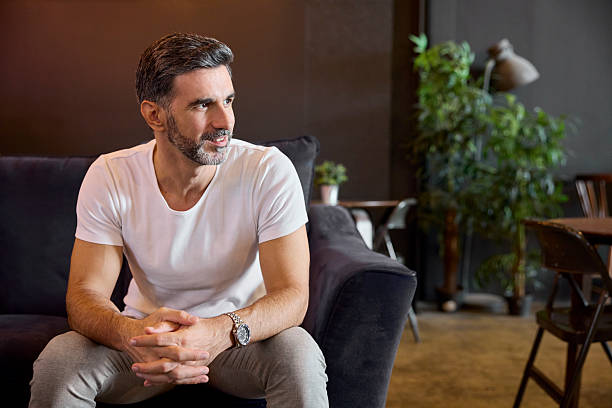 istock Businessman looking away while sitting on sofa at office. Freelancer with beard is wearing wristwatch. He is contemplating. 2213038351