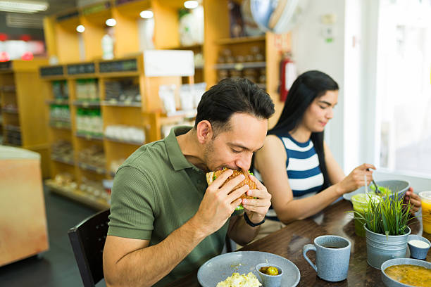 istock Hispanic man eating a sandwich at a restaurant with his girlfriend 2213038968