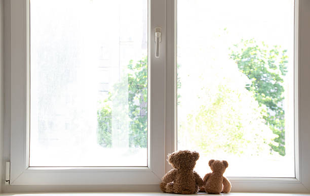 istock Two teddy bears sit on a windowsill by a window in a sunny apartment, looking out 2213039632