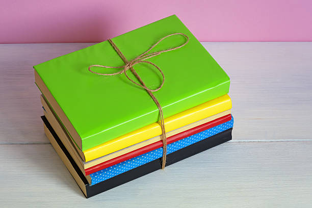 Stack of colorful books tied with rope on white rustic table. Copy space