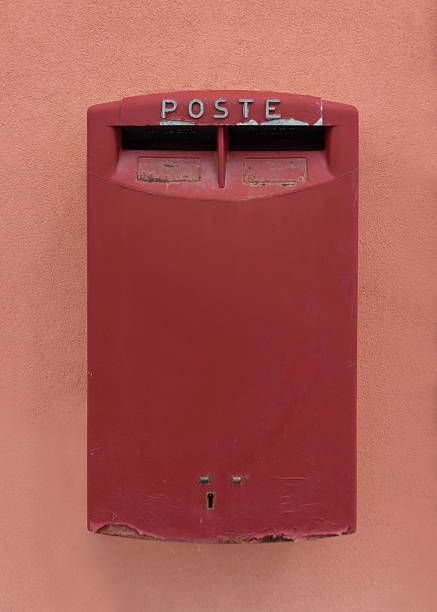 Old red mailbox with inscription POSTE mounted on pastel peach wall in Italy showing classic postal design