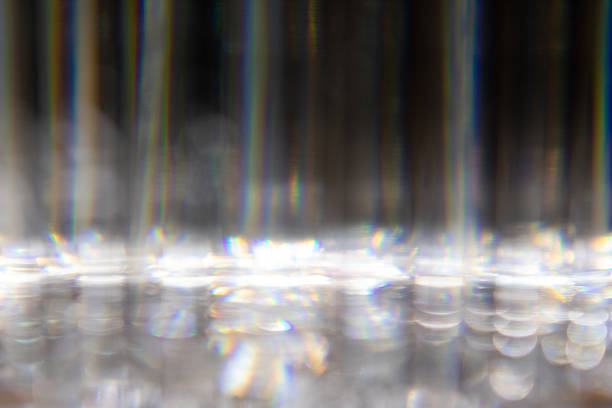 Abstract close-up featuring blurred radial patterns with a strong light source, possibly from a lamp with a ridged surface. The image shows various shades of gray and white with hints of iridescence, suggesting reflections or refracted light. The texture appears glossy, creating a visual rhythm of lines converging towards a bright focal point, lending a dynamic sense of depth and movement.