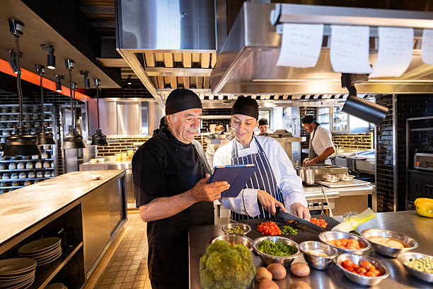 Chef using a tablet and giving instructions to a cook while working at a commercial kitchen - restaurant concepts