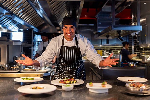 Happy Latin American chef presenting plates at a restaurant with his arms open and smiling - food and drink concepts