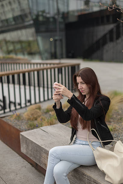 istock A woman sits on a bench, taking a selfie with her phone 2213060759