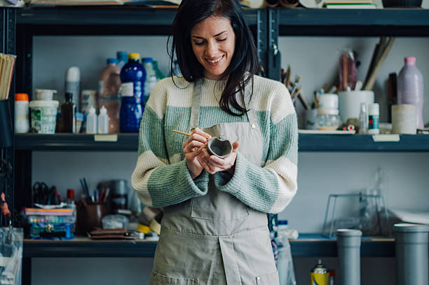 istock Smiling female artisan painting a clay cup in her workshop 2213062522