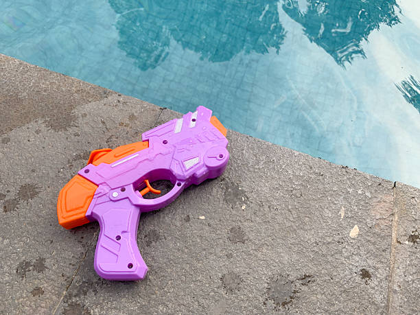 A colorful water gun toy placed on the edge of a swimming pool, evoking playful summer vibes and outdoor fun
