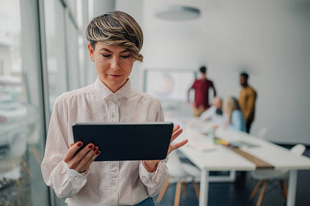 istock Businesswoman using digital tablet in modern office with colleagues working in background 2213076894