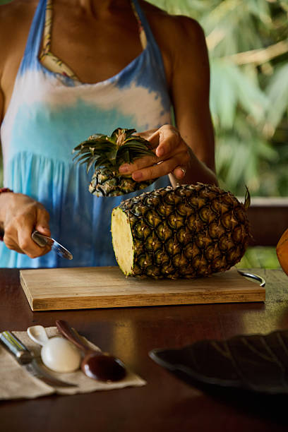 istock Woman slicing a ripe pineapple on a cutting board in tropical setting 2213080003