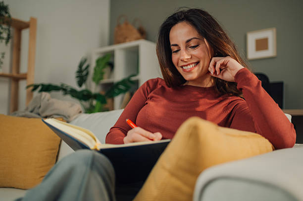 istock Young woman writing on notebook sitting on sofa at home 2213080587