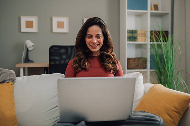 istock Young woman working remotely from home using laptop on sofa 2213080590