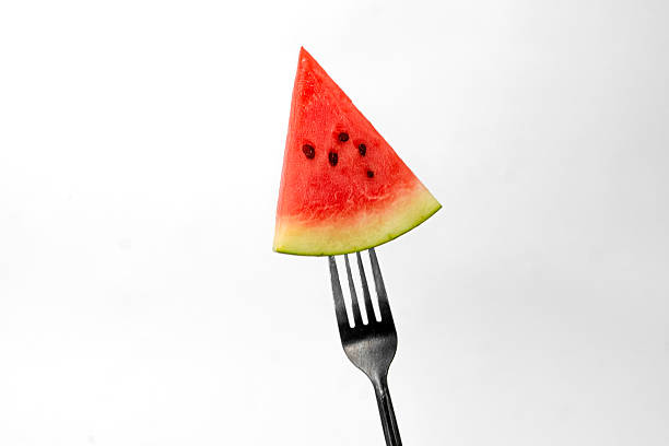 A fresh triangular slice of watermelon with seeds pierced on a silver fork, isolated on a white background. A vibrant and juicy tropical fruit perfect for summer refreshment.