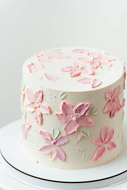 Birthday, wedding or anniversary cake with white cream cheese frosting and decorated with pink cream flower petals. White background
