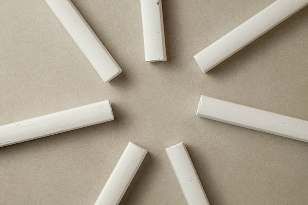 Several white chalk sticks are arranged in a circular pattern on a light brown background. Soft natural light highlights their texture and simplicity, evoking a sense of artistic potential.