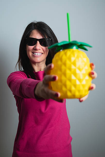 Smiling woman offering pineapple shaped drink wearing sunglasses