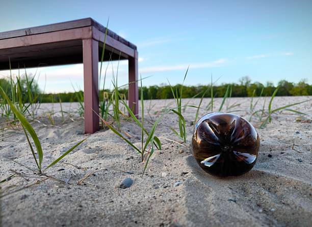 A brown plastic bottle is lying like garbage on the beach, next to a bench for relaxing. A plastic bottle is like trash on the beach. Close up pedestal shot