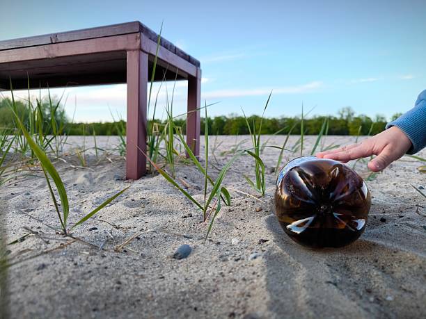 A brown plastic bottle is lying like garbage on the beach, next to a bench for relaxing. A plastic bottle is like trash on the beach. Close up pedestal shot