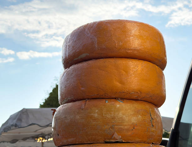 Stack of large orange cheese wheels against blue sky, lifestyle