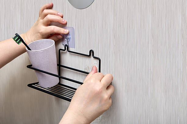 istock Hands are installing black wire bathroom shelf on wall using transparent nano adhesive hook for easy and damage-free bathroom hardware fitting. 2213107981