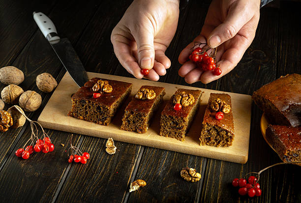 istock A baker arranges four slices of moist cake on a wooden platter, adding red berries and walnuts as a garnish. The rustic kitchen features dark wood and natural lighting 2213108346