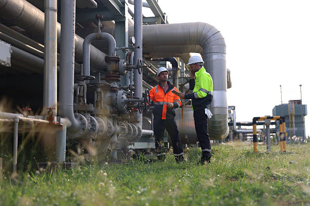 istock Two Male technicians wearing reflective safety jackets and hard hats are working outdoors in an industrial place of work with chemical plant piping. 2213121197