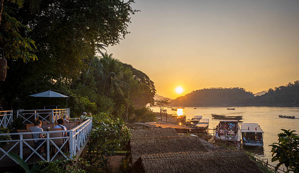 Luang Prabang, Laos - November 9, 2024：A relaxing evening scene by the Mekong River in Luang Prabang, Laos, with people enjoying the view as the sun goes down.